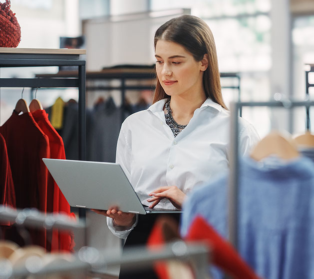 A clothing store attendant standing by clothing racks looking over inventory on her iPad